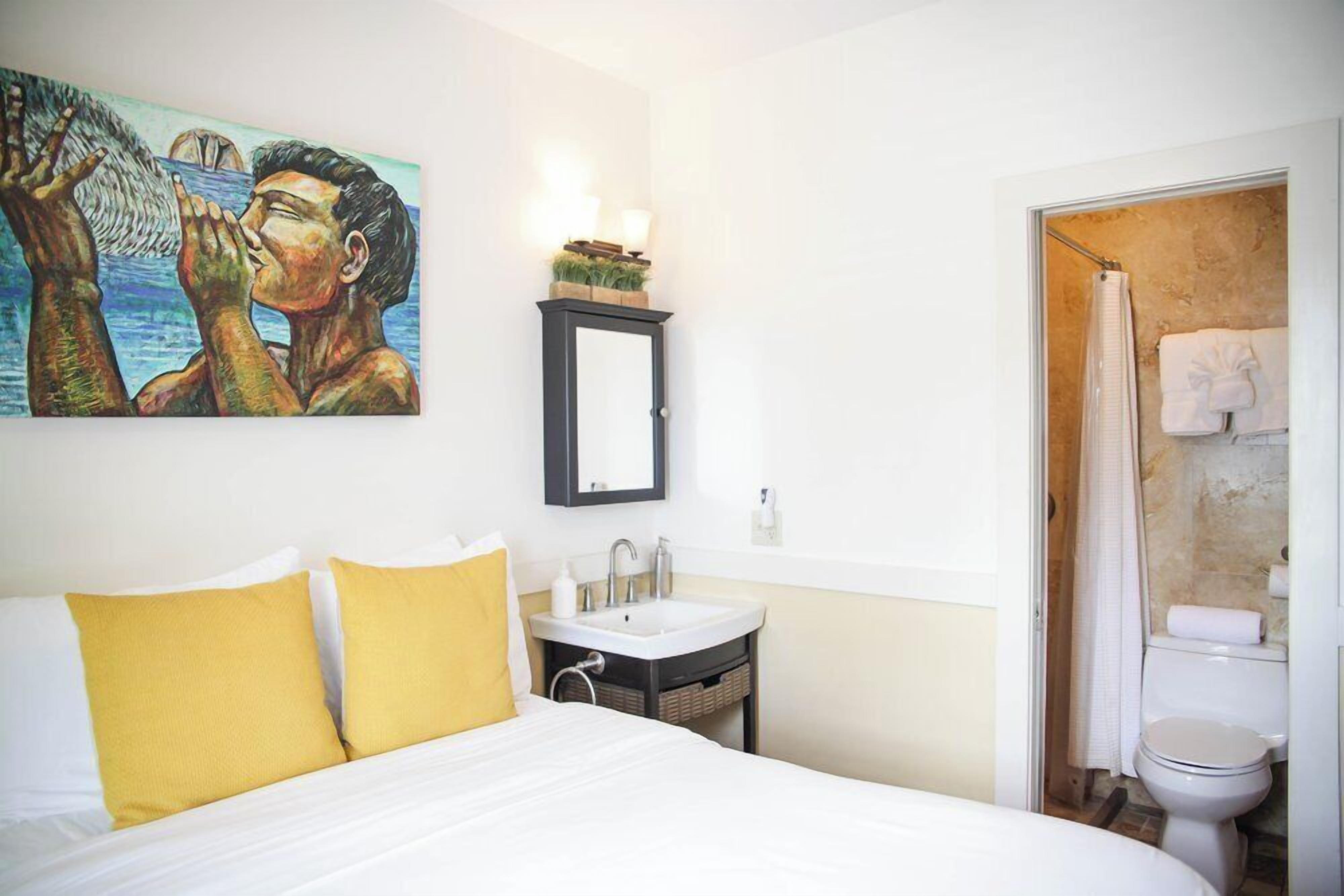 A hotel room with a bed, a sink, a mirror, and a shower.