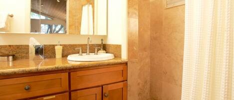 A bathroom with a granite countertop, a white sink, and wooden cabinets.