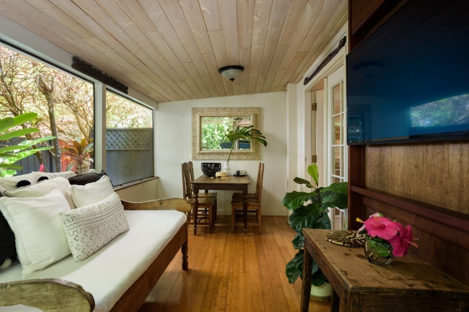Une pièce chaleureuse avec un plafond en bois, une table à manger avec des chaises, un canapé avec des coussins et une grande fenêtre donnant sur les arbres.