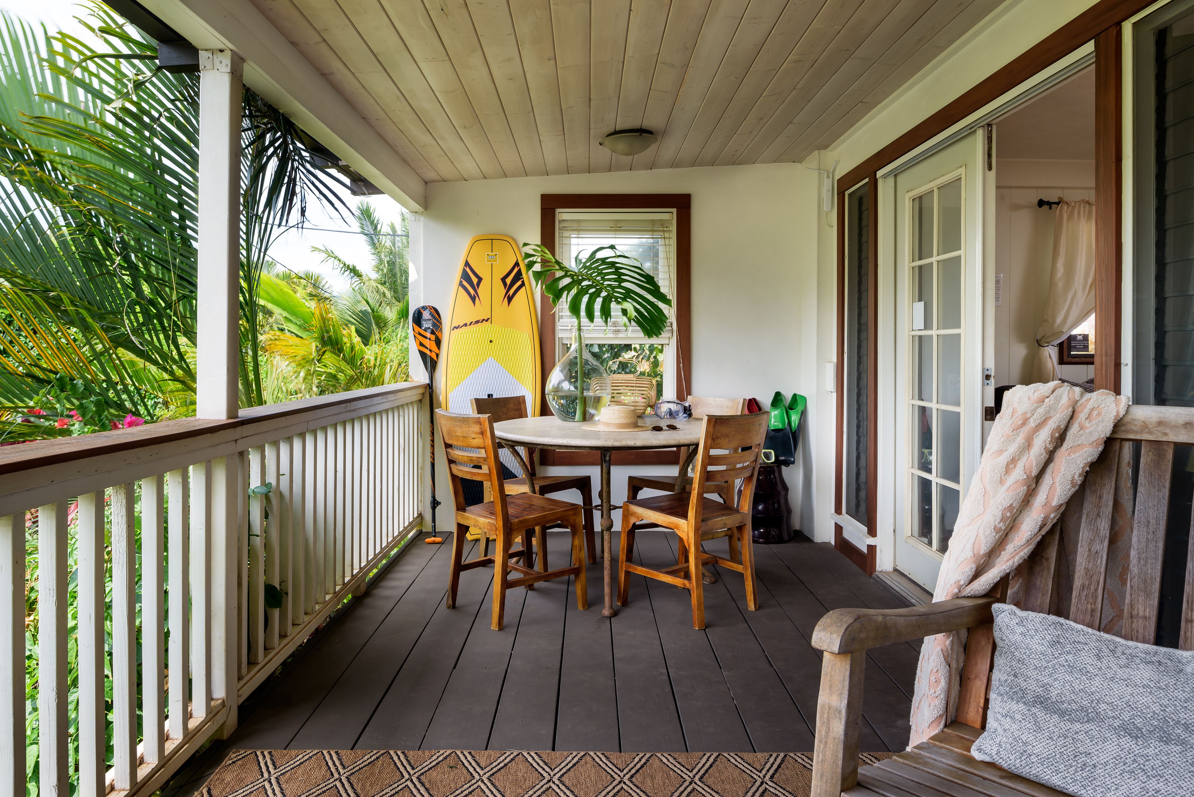 A wooden deck with a table and chairs, a surfboard, and a potted plant.