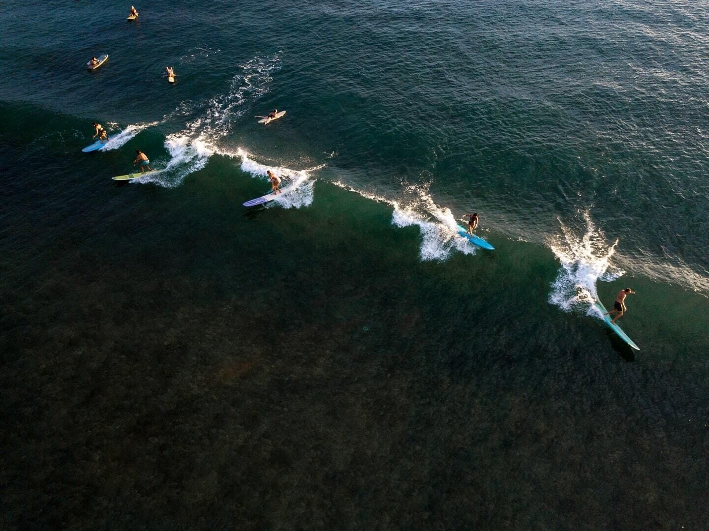 An aerial view of a beach with multiple surfers and a jet ski.