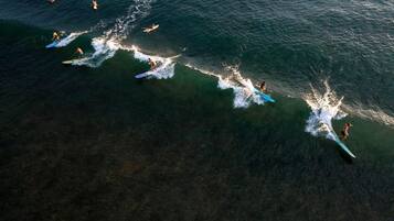 An aerial view of a beach with multiple surfers and a jet ski.