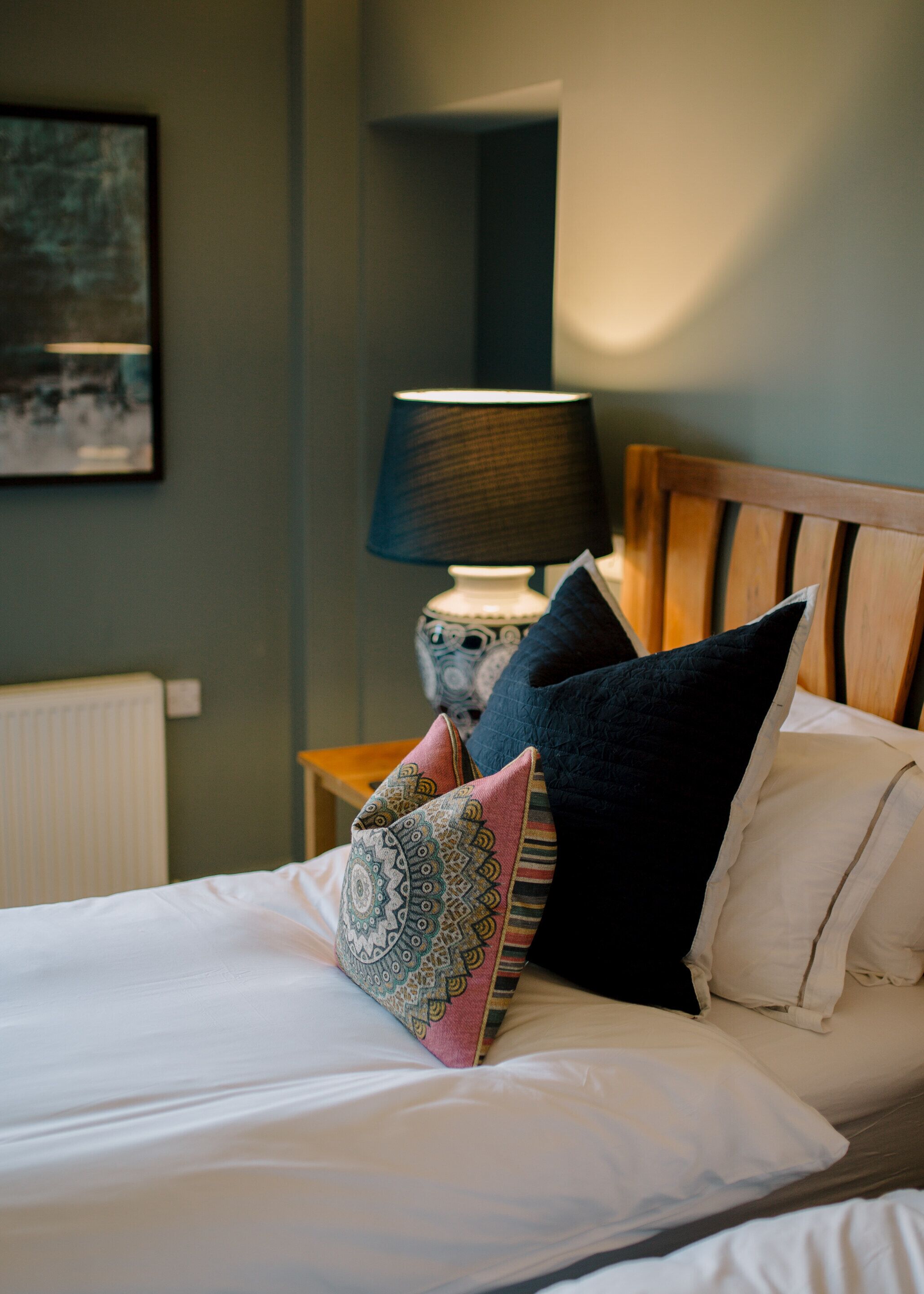 A neatly made bed with patterned pillows and a bedside lamp.