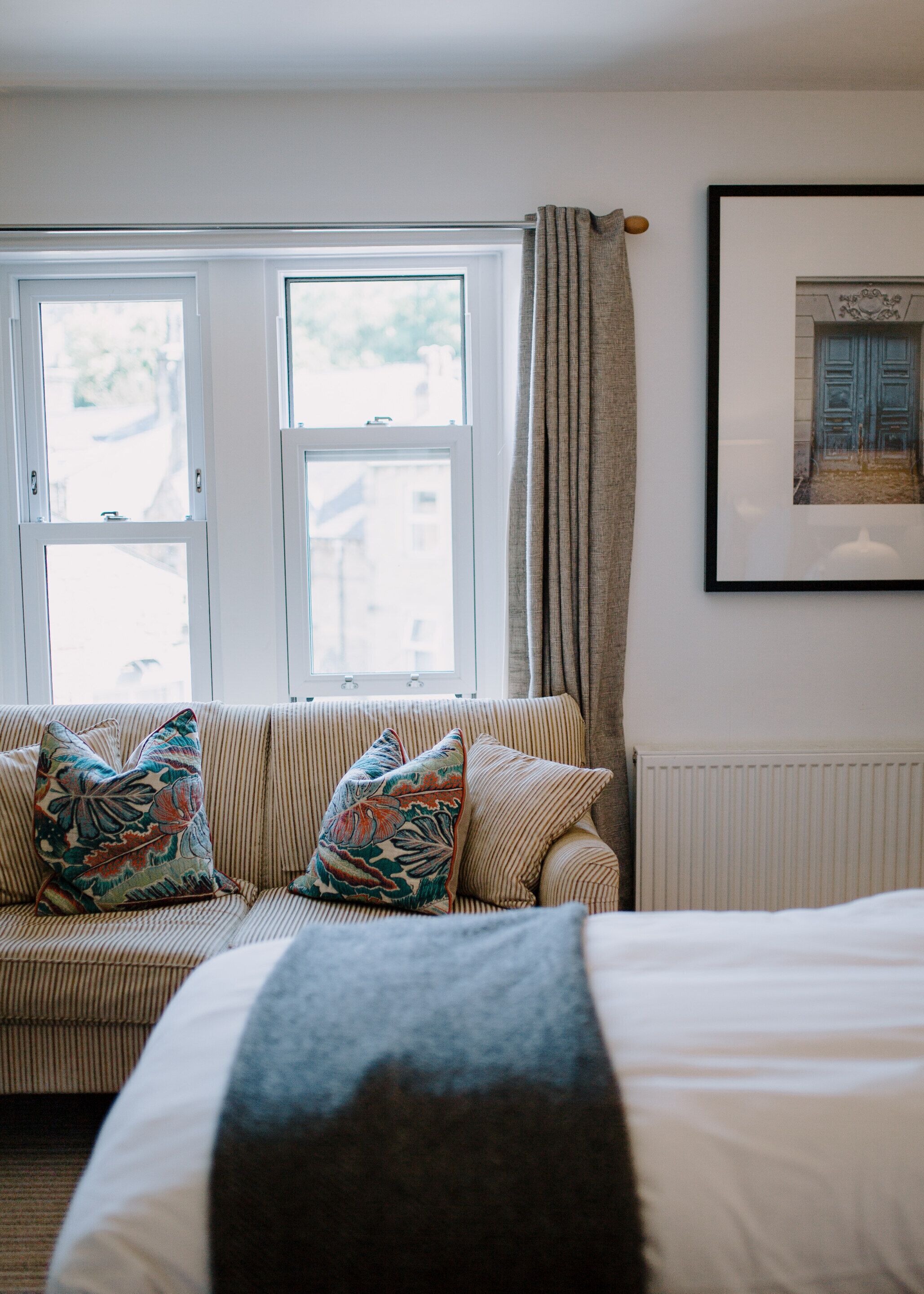 A room with a striped sofa, a bed, a framed picture on the wall, and a window with curtains.