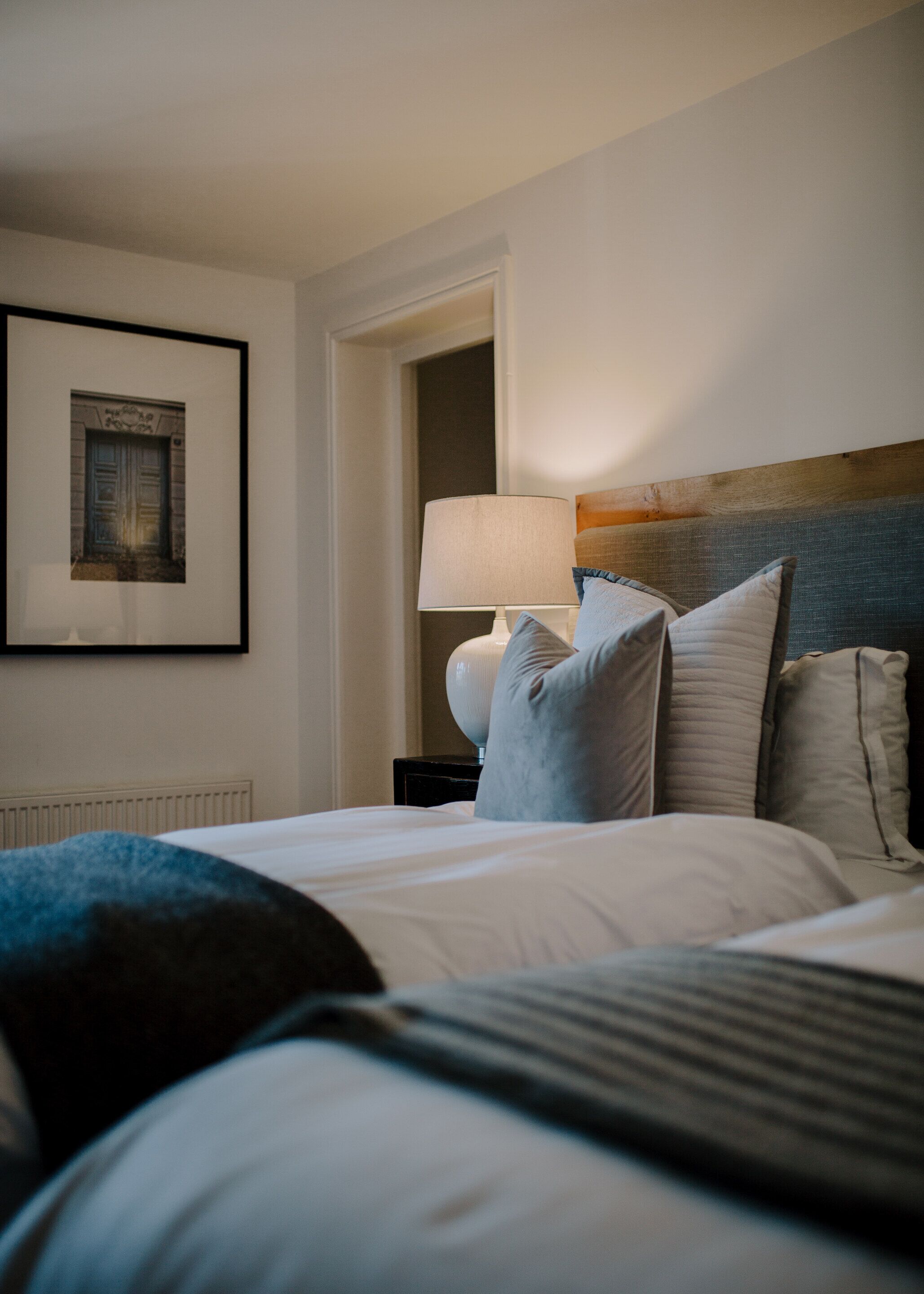 A hotel room with a neatly made bed, a lamp on a bedside table, and a framed picture on the wall.