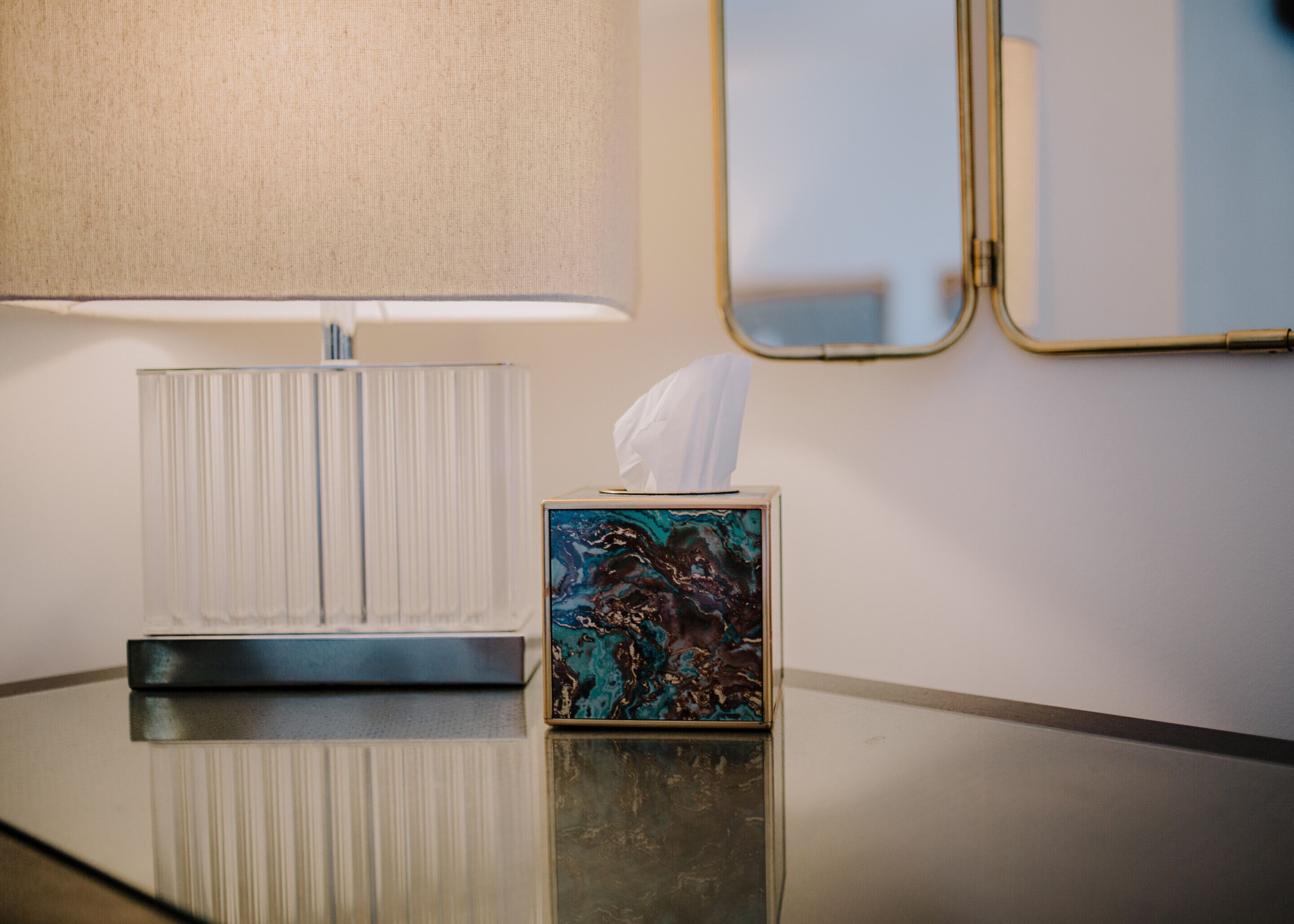 A hotel room with a bedside table, a lamp, a tissue box, and a mirror.