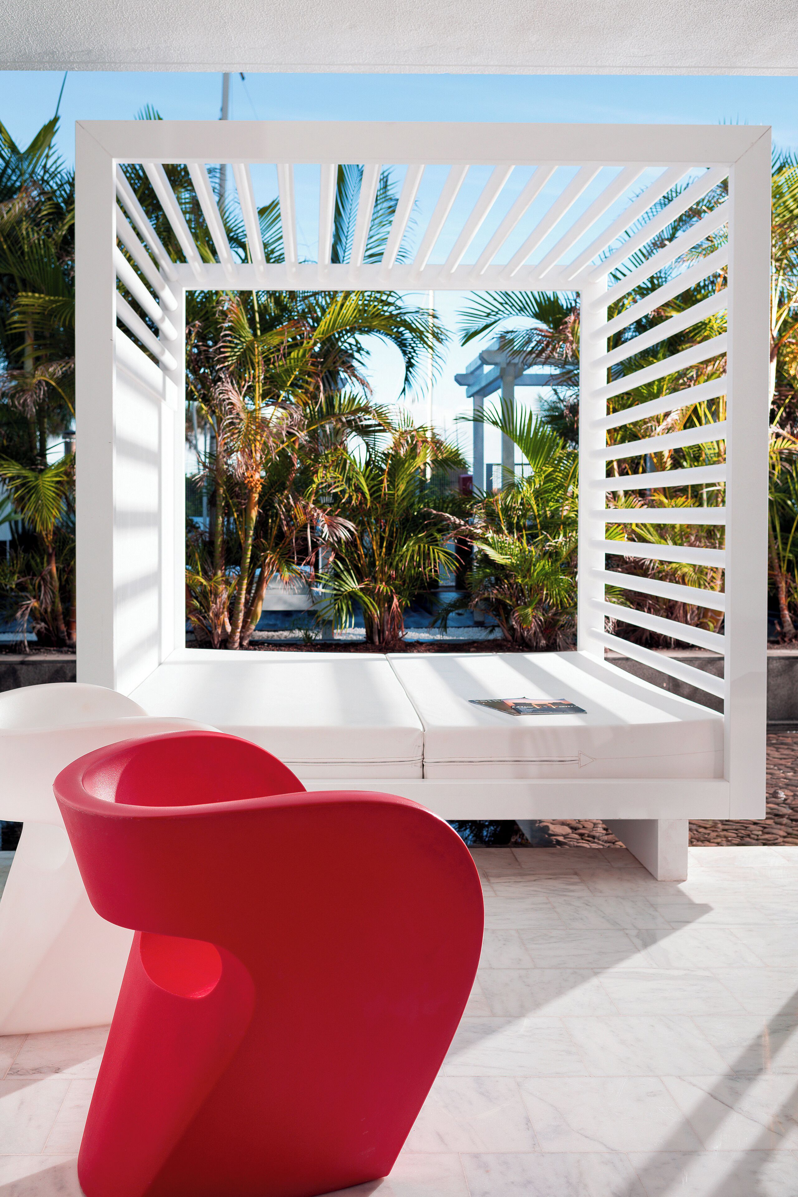 Un área de estar exterior blanca con vistas a palmeras y una piscina.