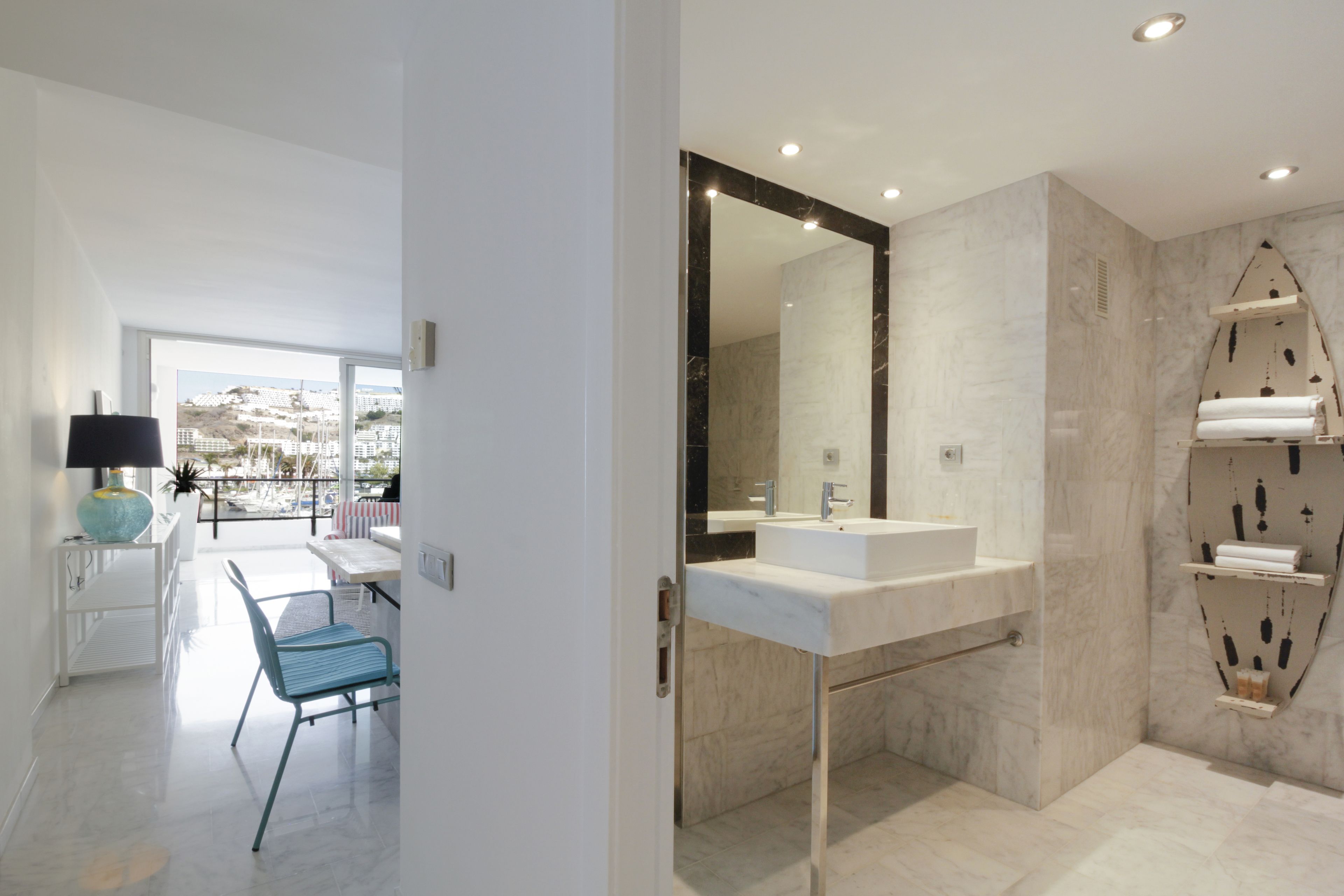 Un baño moderno con un espejo grande, lavabo blanco y paredes de mármol.