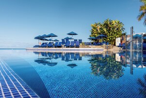 Una piscina al aire libre, sombrillas, sillones reclinables de piscina