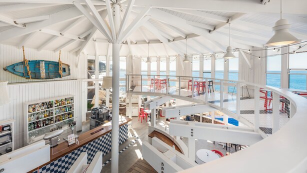 Un interior de varios niveles con una escalera central, una zona de bar y áreas de estar con vistas al mar.