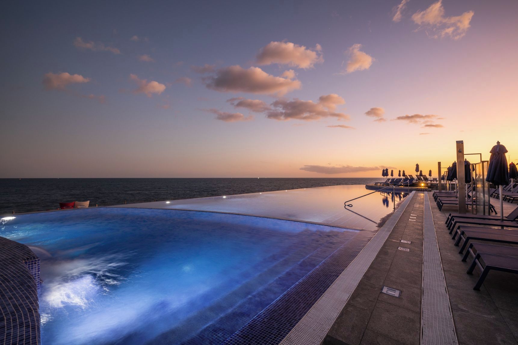 Una piscina infinita con vistas al océano al atardecer.