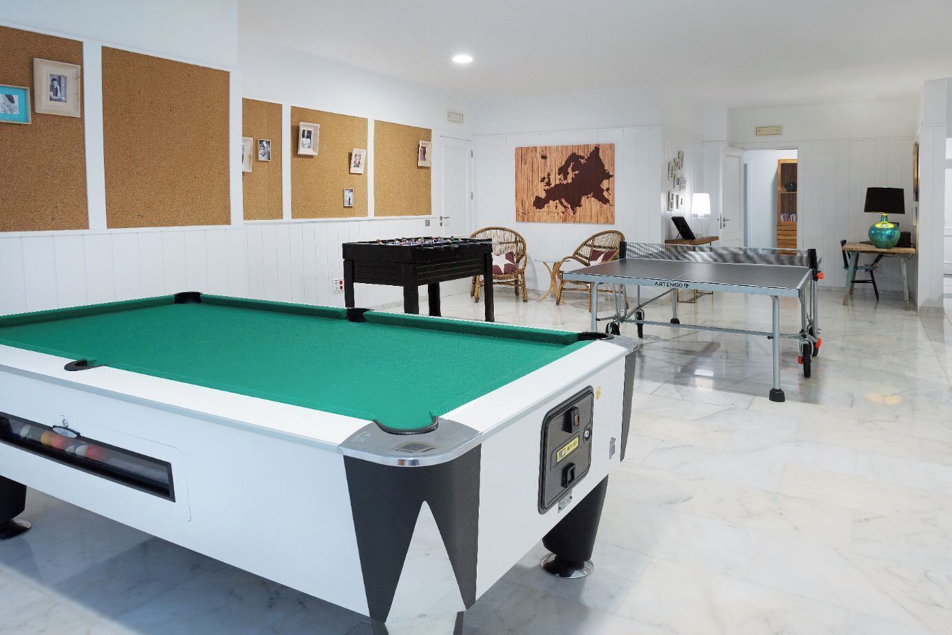 A pool table in a room with a corkboard wall, a map, and a table tennis table.