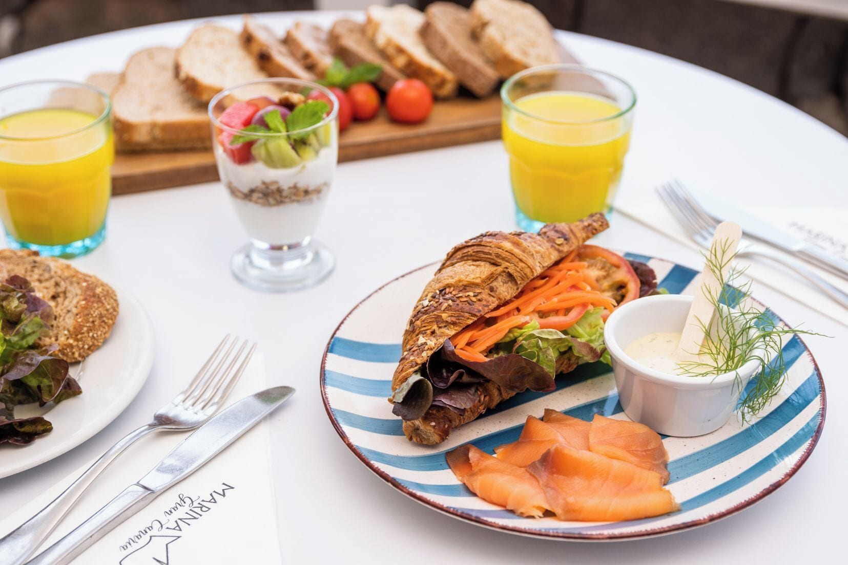A breakfast setting with croissants, smoked salmon, and a salad on a plate, accompanied by juice and bread.