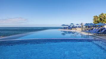 Relax by the serene infinity pool overlooking the ocean, surrounded by lounge chairs and umbrellas.