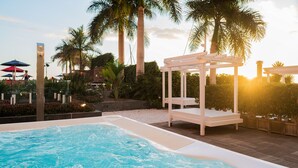 Una piscina con hidromasaje, rodeada de palmeras y una pérgola.