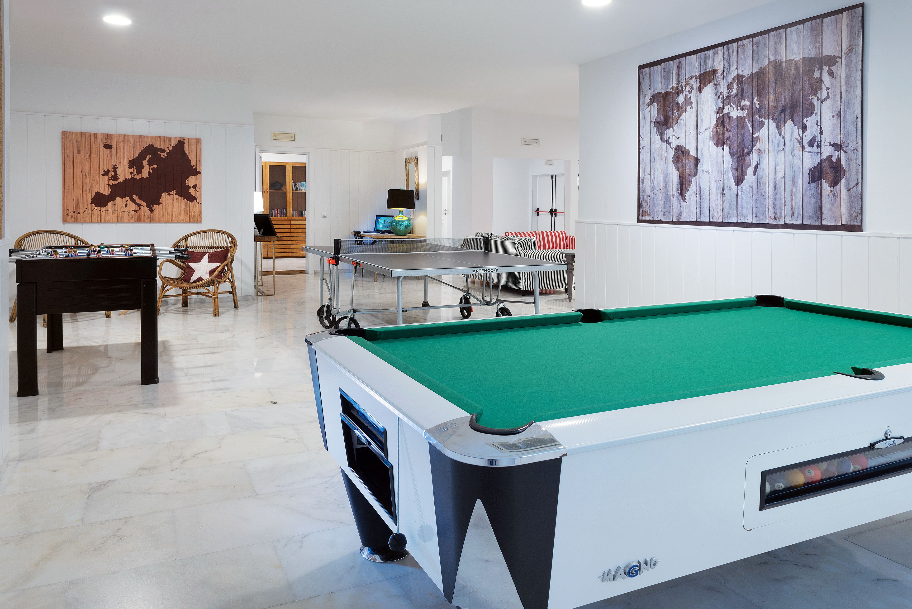 A pool table with a green felt surface, a foosball table, and a billiards table in a room with white walls and a wooden floor.