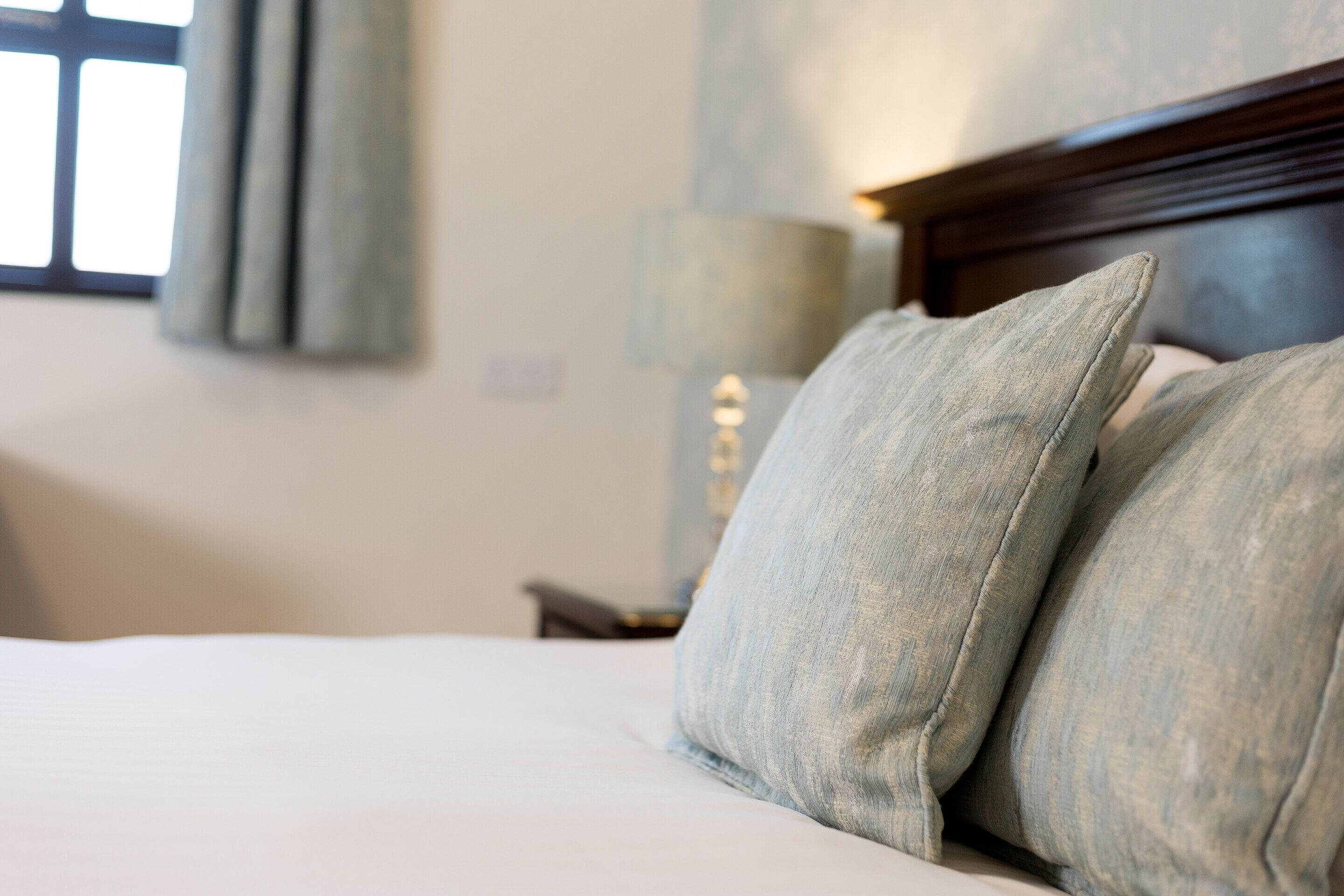 A neatly made bed with a wooden headboard and a lamp on a bedside table.