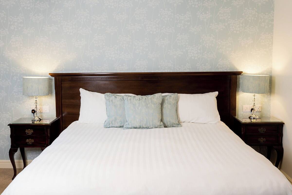 Un letto rifatto con cura, con una testiera in legno, due comodini con lampade e una carta da parati a motivi floreali.