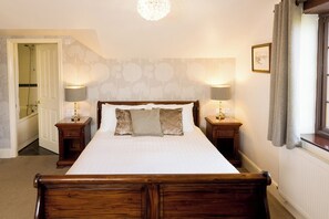 A bedroom with a large bed, two bedside tables with lamps, a wooden headboard, a radiator, and a window with curtains.