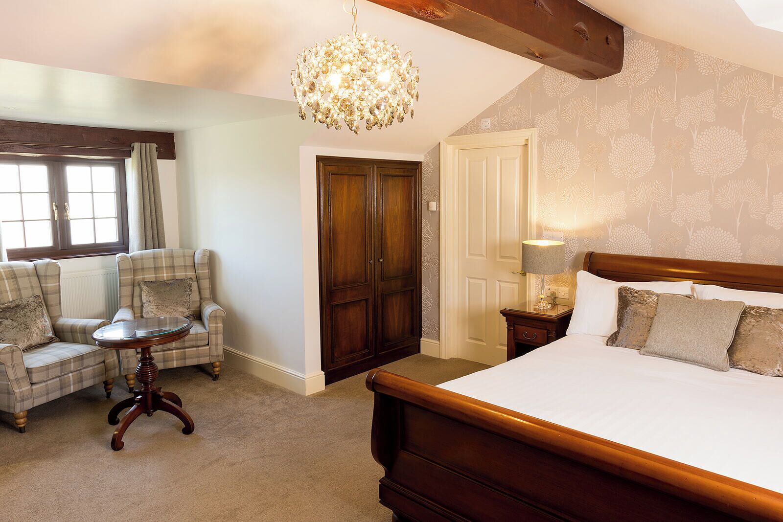 A bedroom with a bed, a chair, a small table, a chandelier, and a wardrobe.