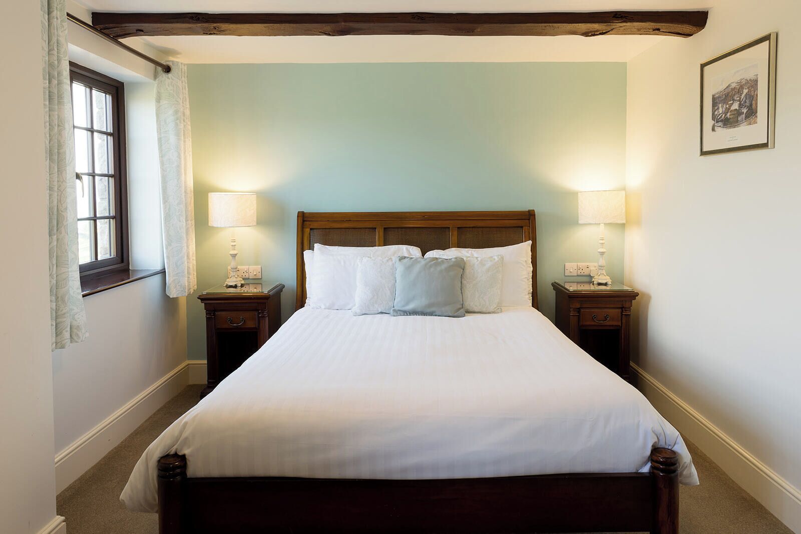 A neatly made bed with white linens in a room with light green walls, wooden headboard, and two bedside lamps.