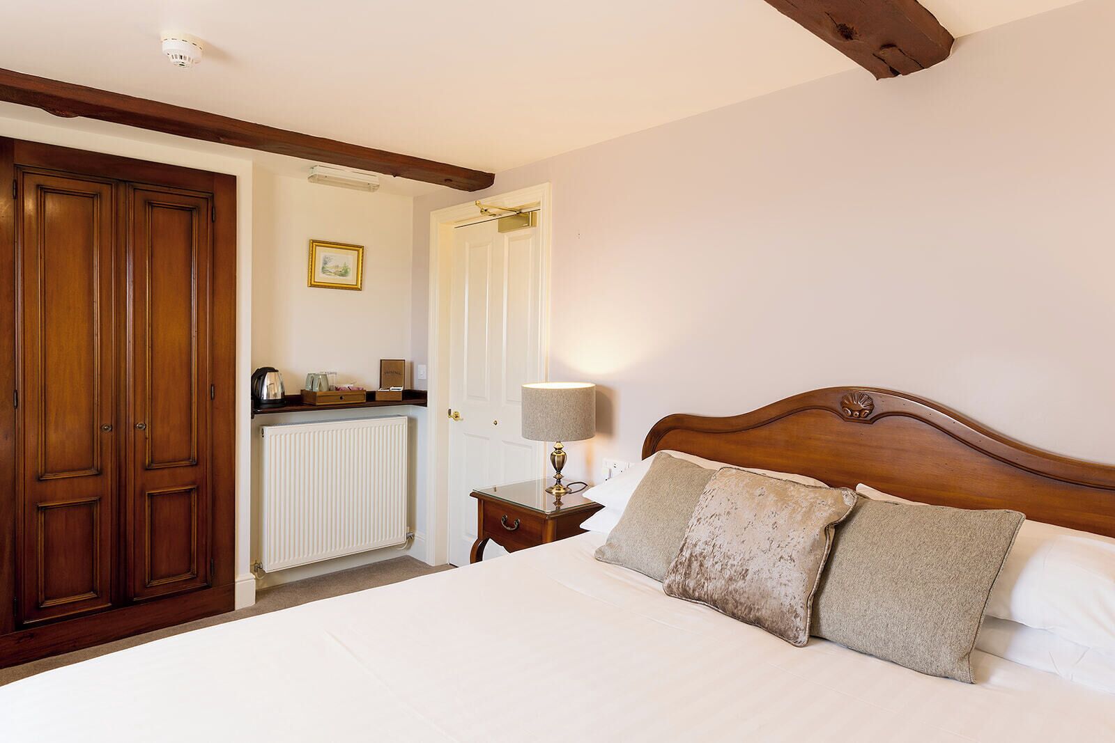 A bedroom with a wooden headboard, a bedside table with a lamp, a radiator, and a wardrobe.