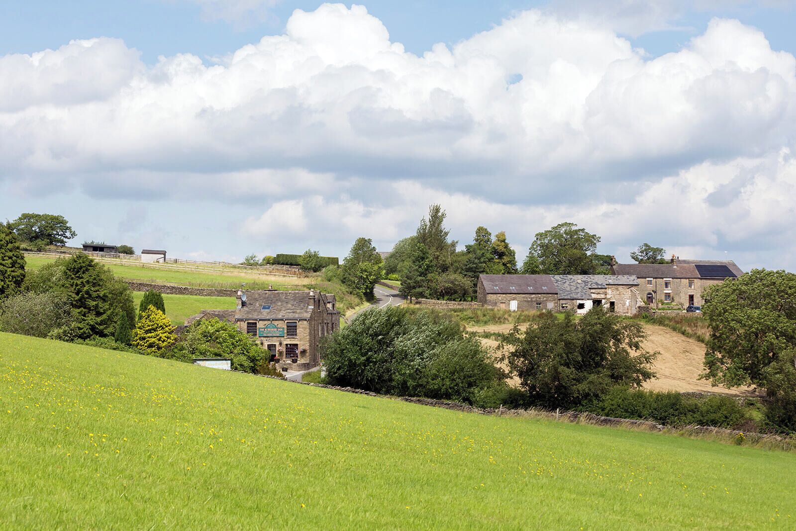 A rural landscape with stone buildings, a grassy field, and a clear sky.