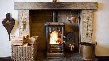 A stone fireplace with a wood-burning stove, a metal kettle, and a basket of firewood.