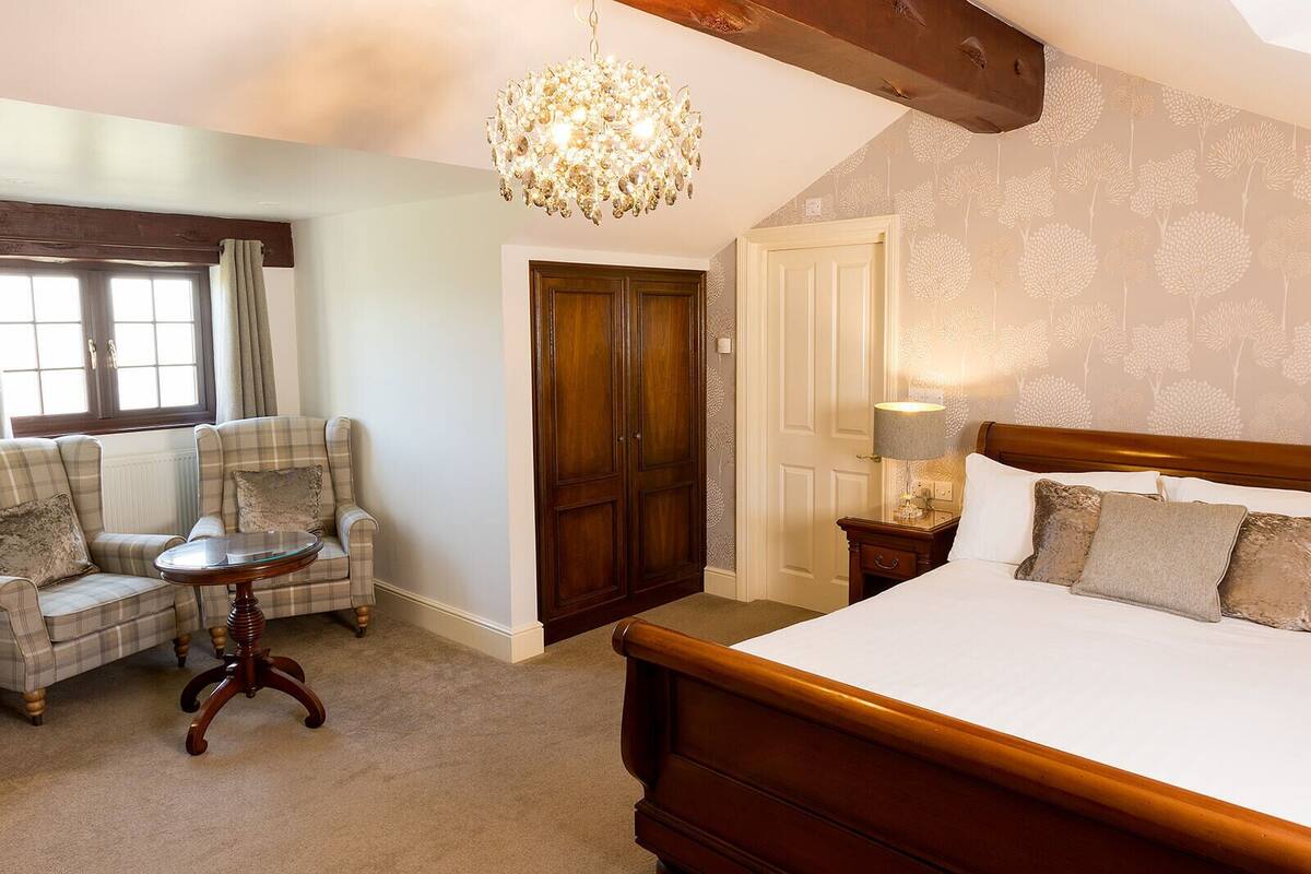 Una camera da letto con un letto grande, una testiera in legno, un lampadario, un divano a quadri, un tavolino rotondo e un armadio.
