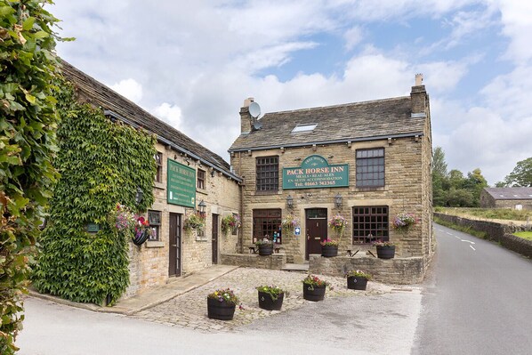A traditional stone building with signs for 'Pack Horse Inn' and 'Pack Horse Inn Meals, Real ales, En-suite Accommodation.'
