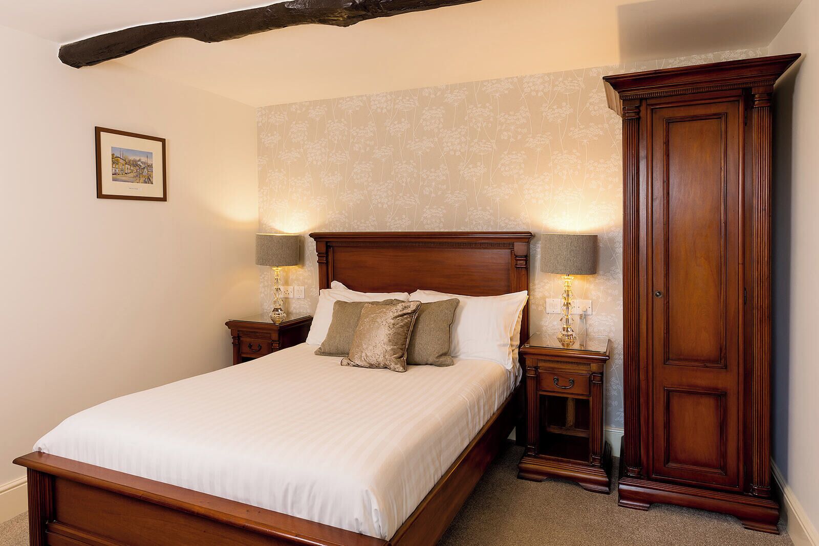 A bedroom with a wooden bed, two bedside tables with lamps, a large wardrobe, and a framed picture on the wall.