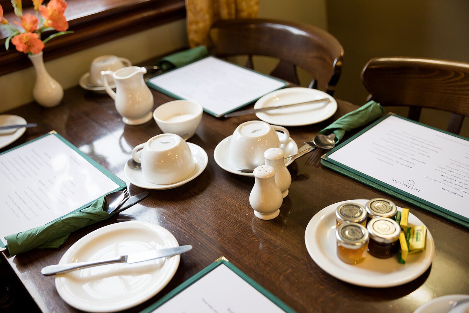 Una mesa de comedor dispuesta con platos, tazones y tazas blancos, además de saleros, pimenteros, una jarra y salsas.