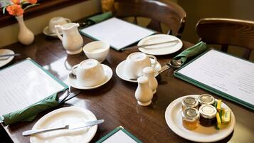 Una mesa de comedor dispuesta con platos, tazones y tazas blancos, además de saleros, pimenteros, una jarra y salsas.