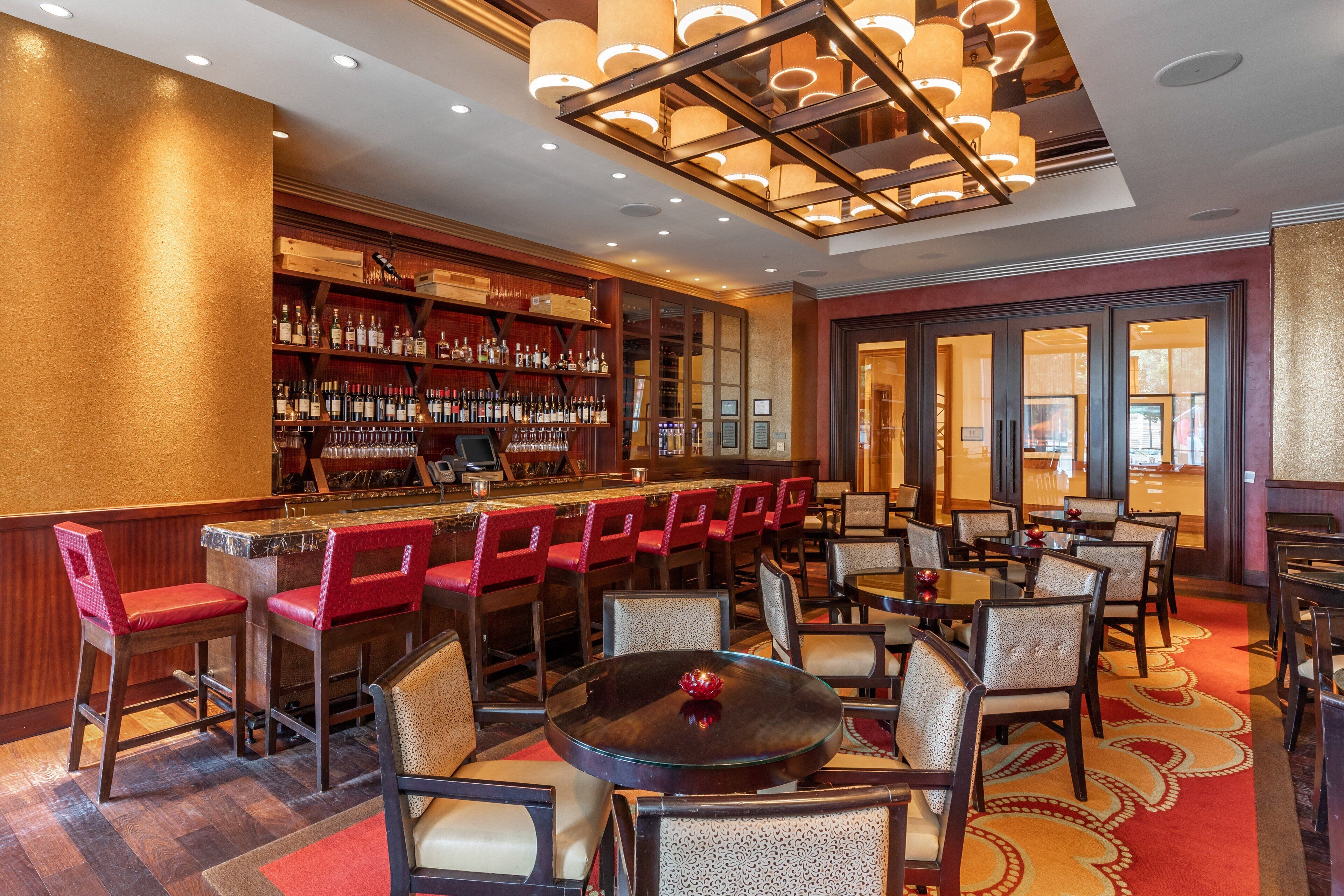 A bar area with multiple seating options, including bar stools and tables, and a well-stocked liquor shelf.