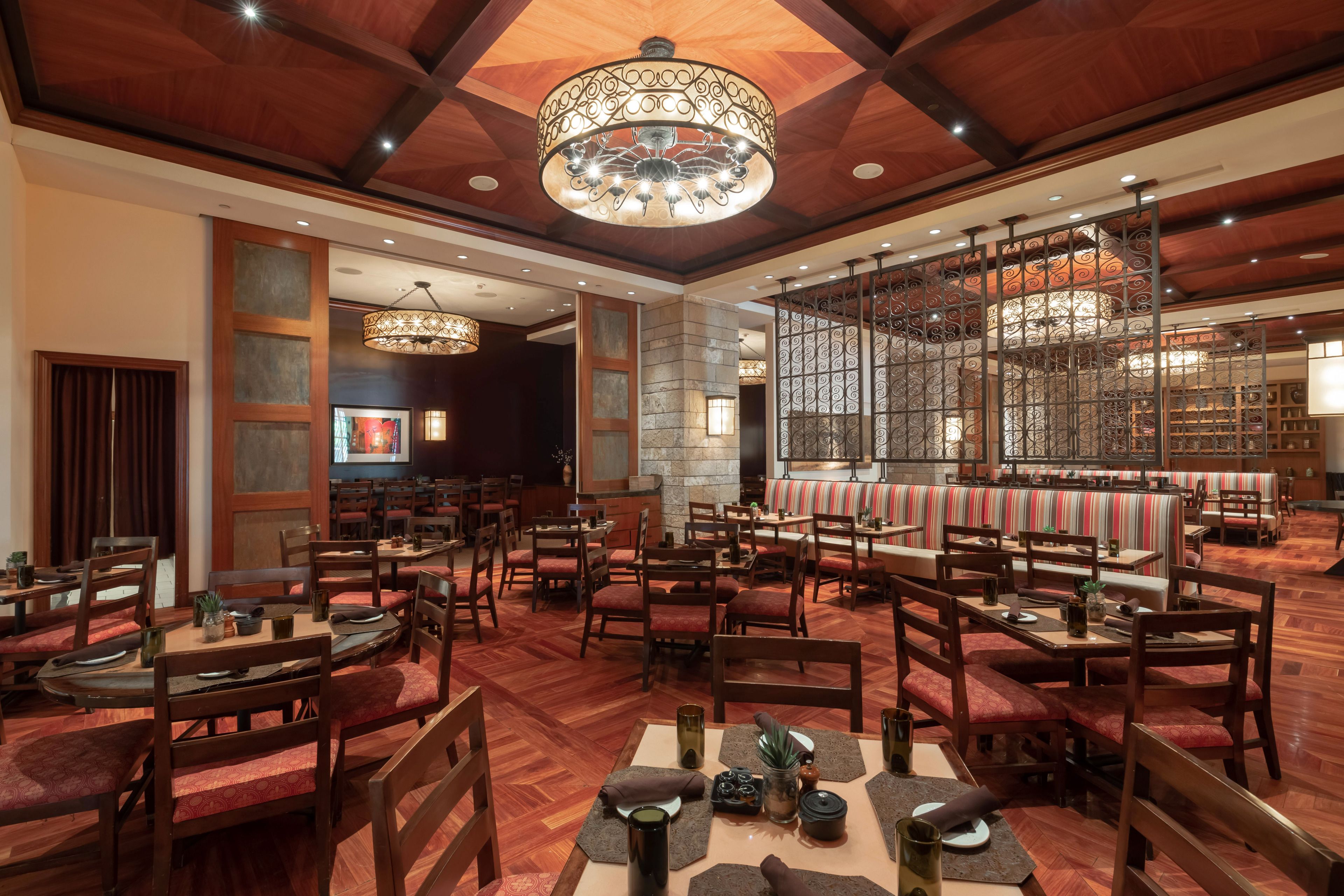 Un restaurant spacieux avec des tables et des chaises en bois, un lustre décoratif et un mur en pierre.