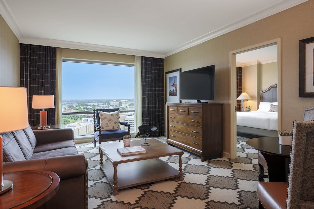 Ein Hotelzimmer mit großem Fenster, Flachbildfernseher, Sofa, Couchtisch, Schminktisch und Bett.