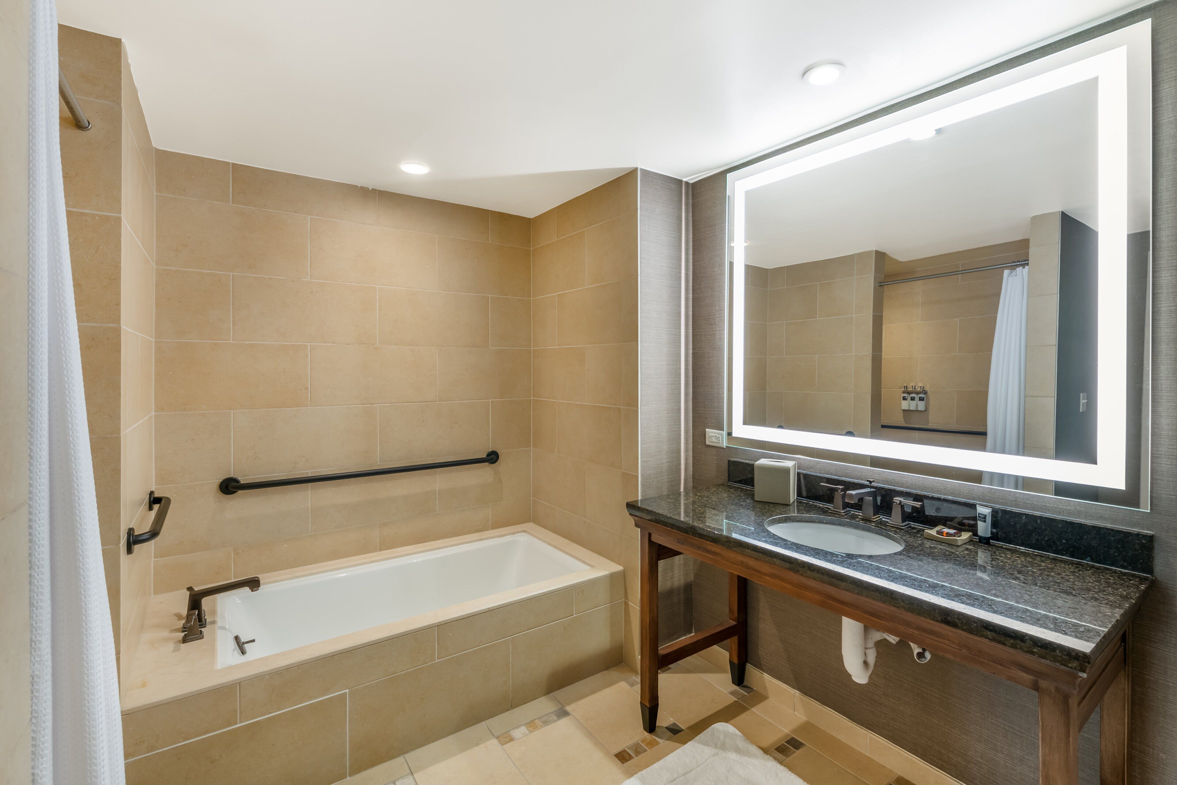A modern bathroom with a bathtub, a vanity with a mirror, and beige tiled walls.