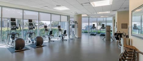 A spacious gym with various exercise equipment, large windows, and a clean, modern design.