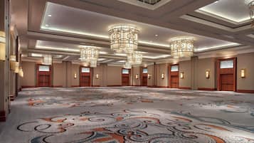 A spacious hotel lobby with a large patterned carpet, multiple chandeliers, and a row of doors.