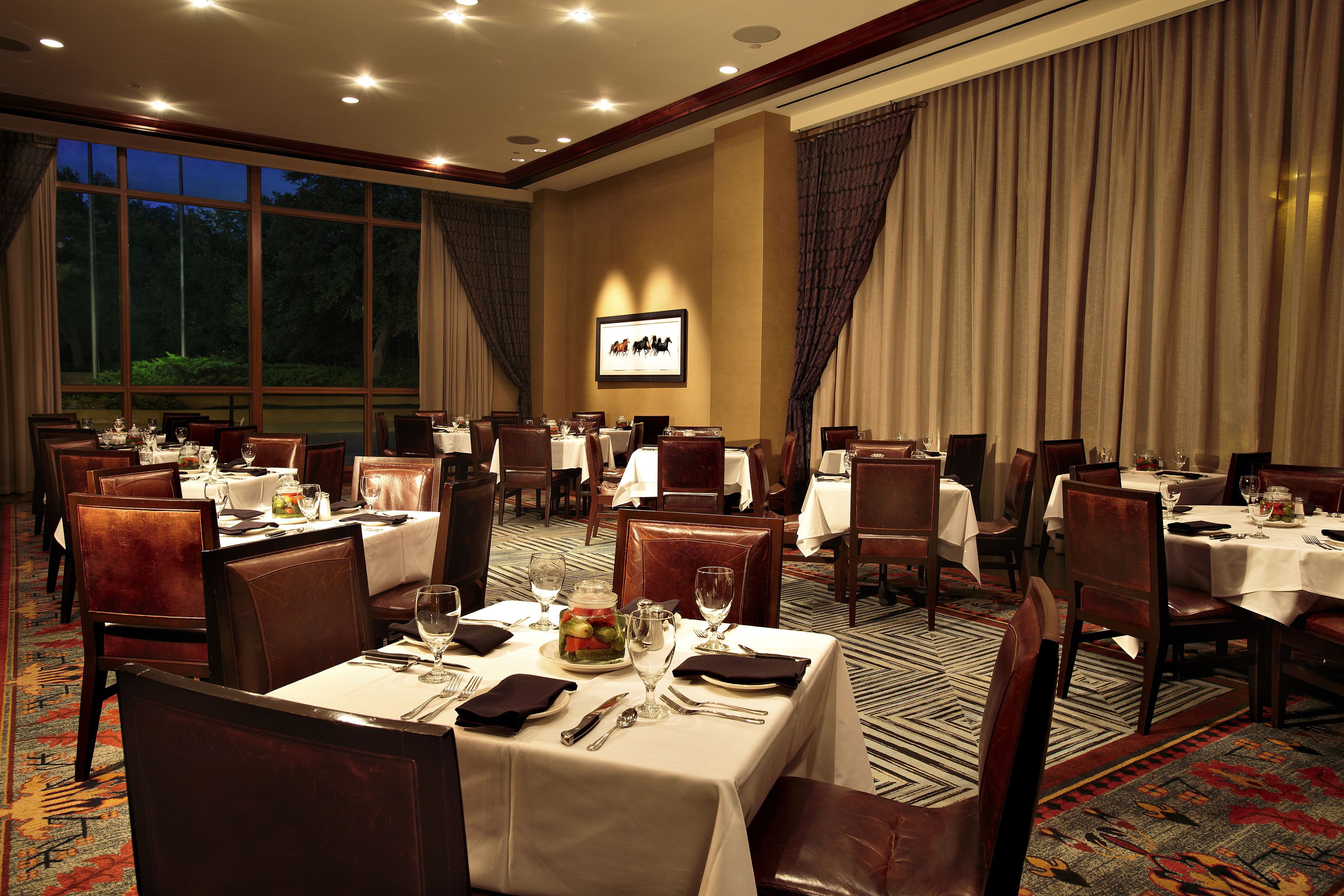 A hotel dining room with multiple tables set for dining, large windows, and a projection screen on the wall.