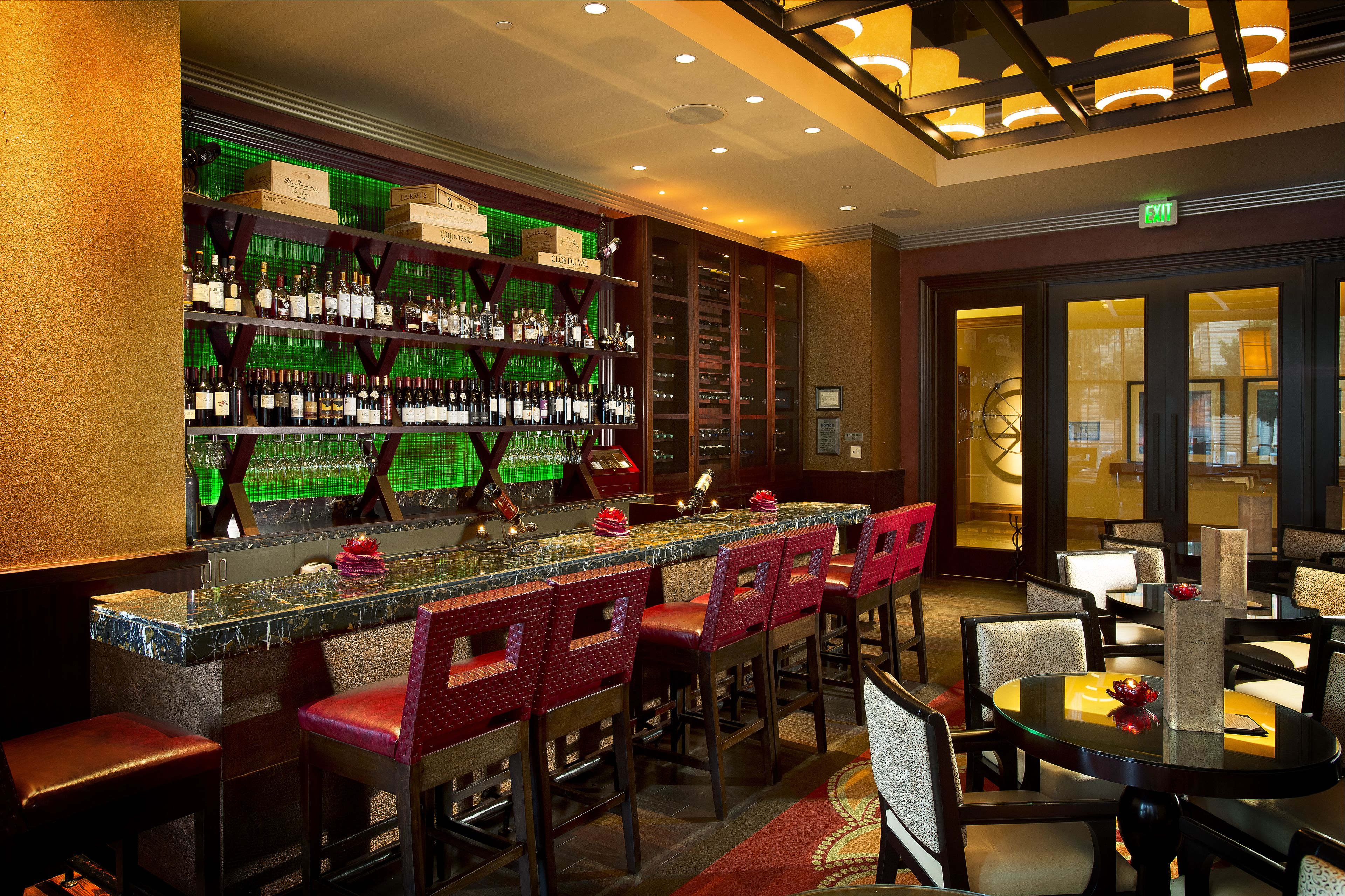 A bar area with a marble countertop, red cushioned bar stools, and shelves stocked with bottles.