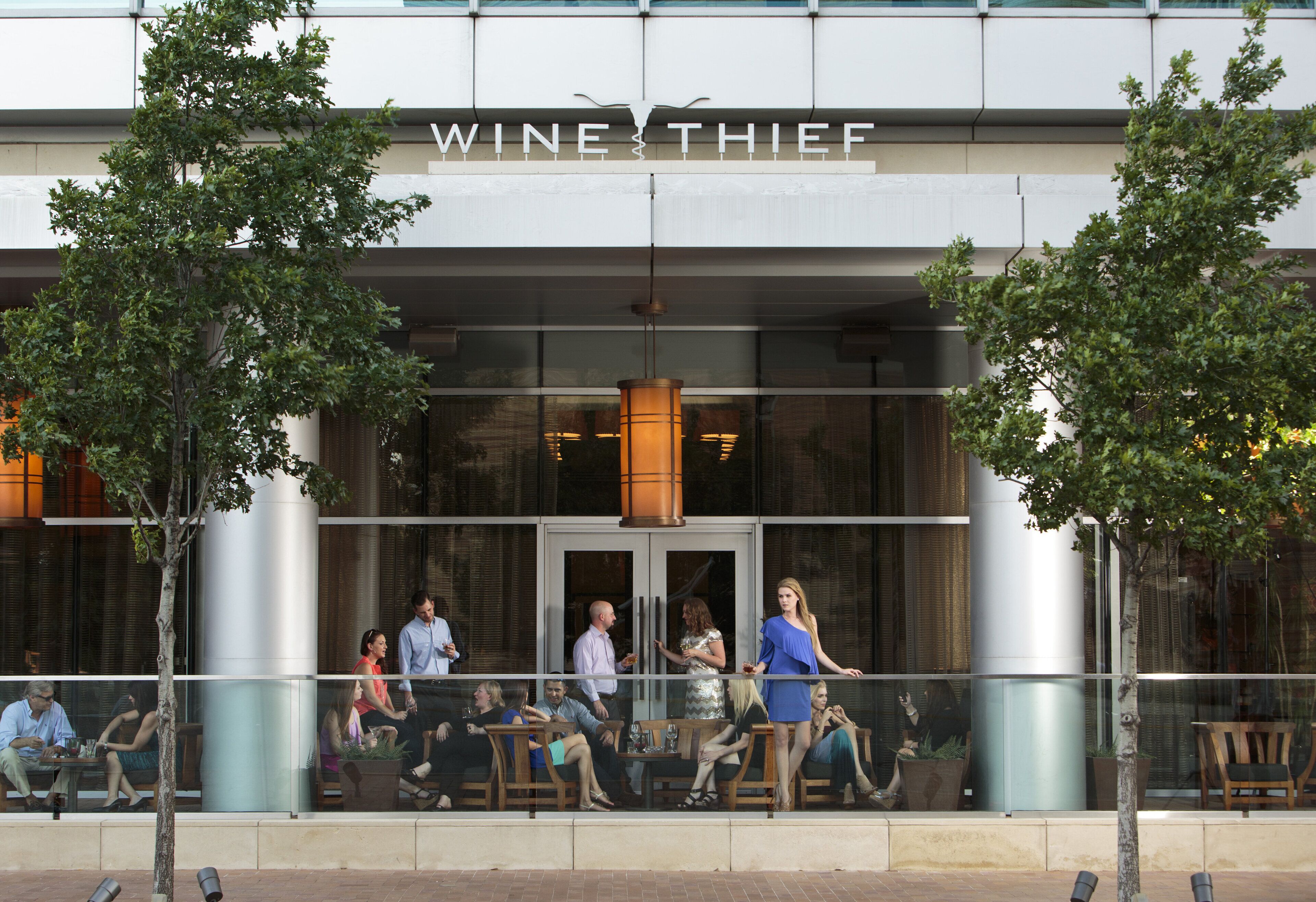 A building with a sign reading "WINE THIEF" and people sitting outside on a balcony.