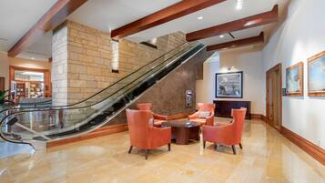 A lobby with a glass elevator, red leather chairs, a marble floor, and a stone wall.