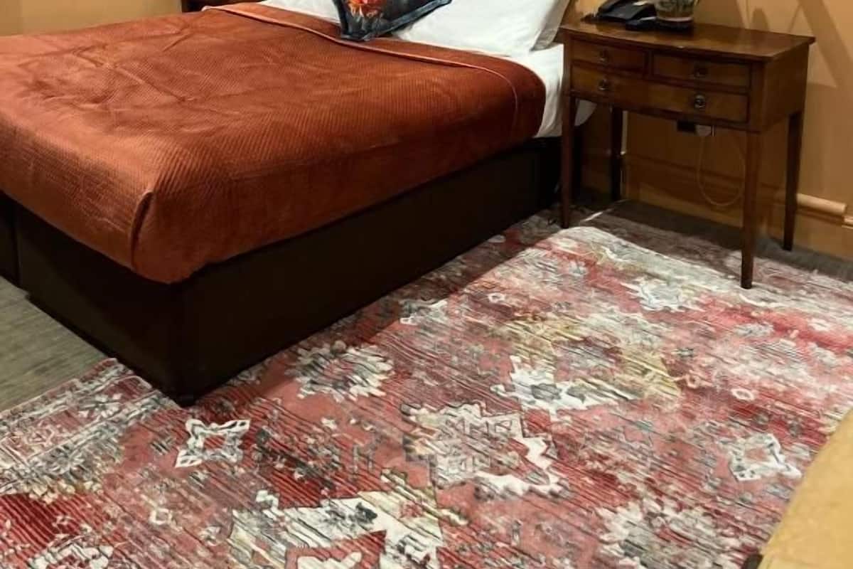 A hotel room with a bed, a nightstand, a lamp, and framed pictures on the wall.