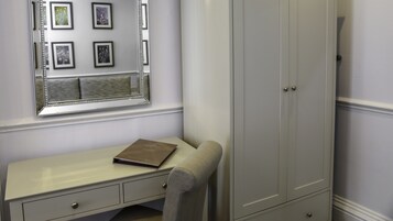Et værelse med et hvidt toiletbord, et spejl med indrammede billeder, en grå garderobe og en brun bog på toiletbordet.