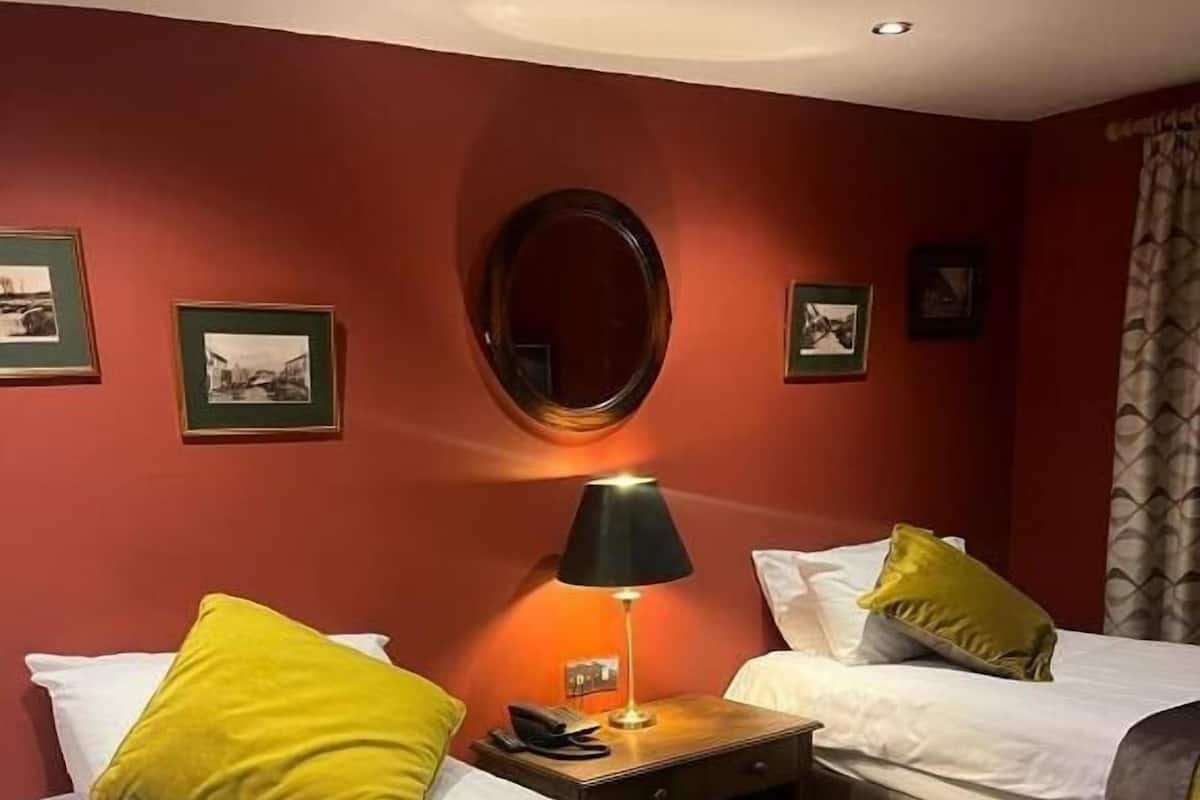 A hotel room with two beds, each with a yellow pillow and a white pillow, a round mirror on the wall, and framed pictures above the beds.