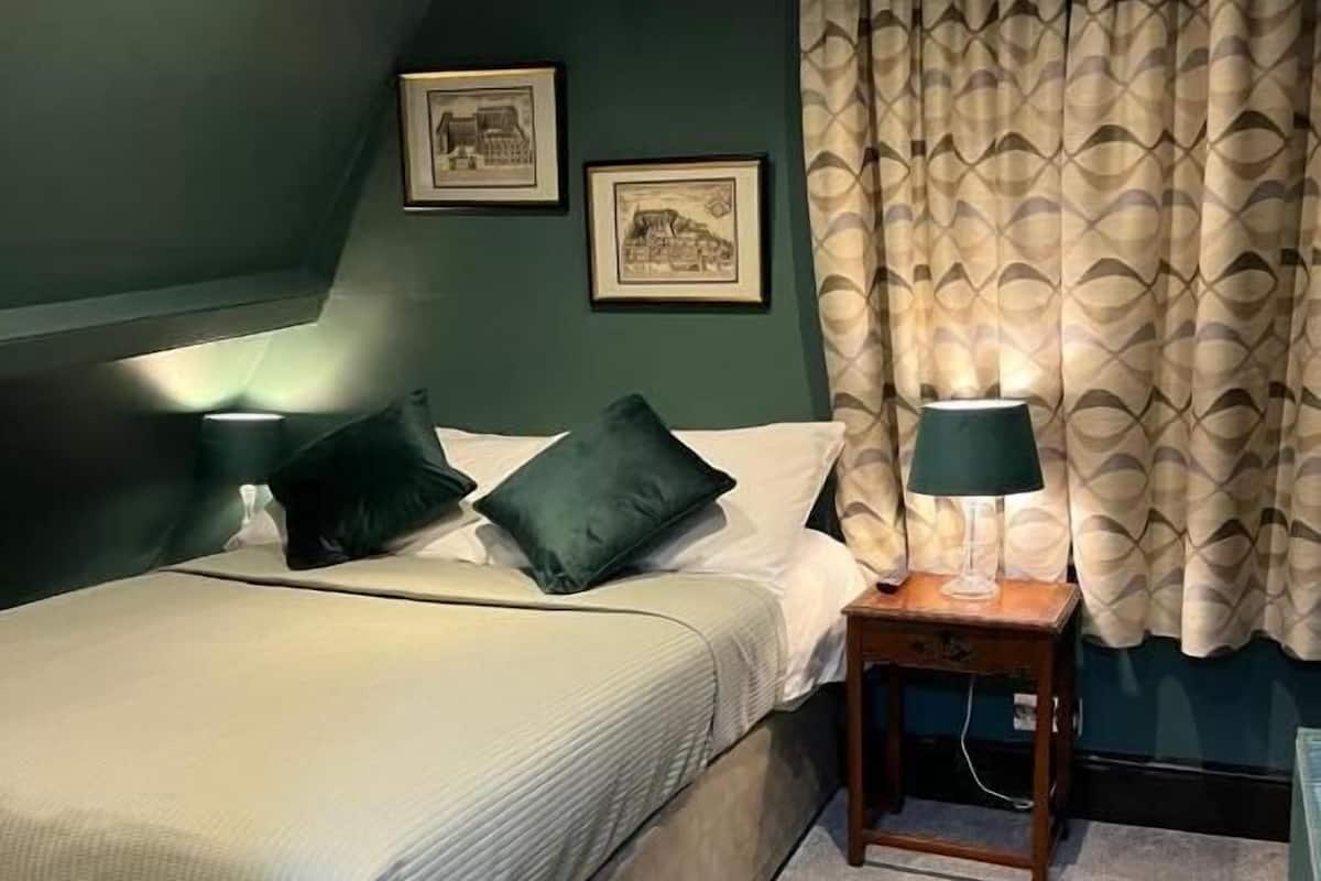 A bedroom with a bed, two pillows, a nightstand with a lamp, and two framed pictures on the wall.