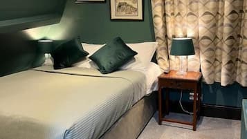 Ein Schlafzimmer mit einem Bett, zwei Kissen, einem Nachttisch mit einer Lampe und zwei gerahmten Bildern an der Wand.