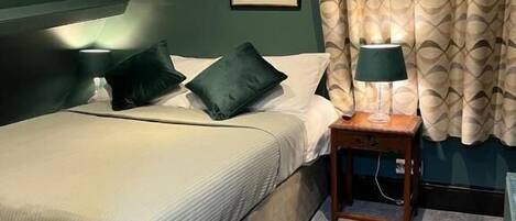 A bedroom with a bed, two pillows, a nightstand with a lamp, and two framed pictures on the wall.
