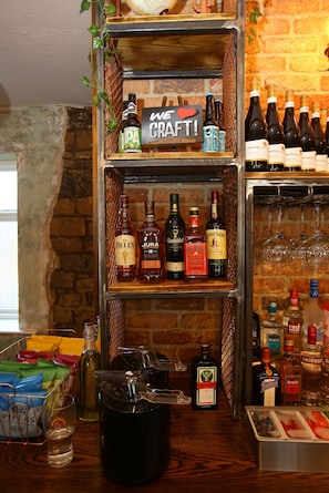 Un'area bar con scaffali pieni di bevande in bottiglia, un cartello con su scritto 'WE LOVE CRAFT!' e diversi bicchieri e bottiglie sul bancone.
